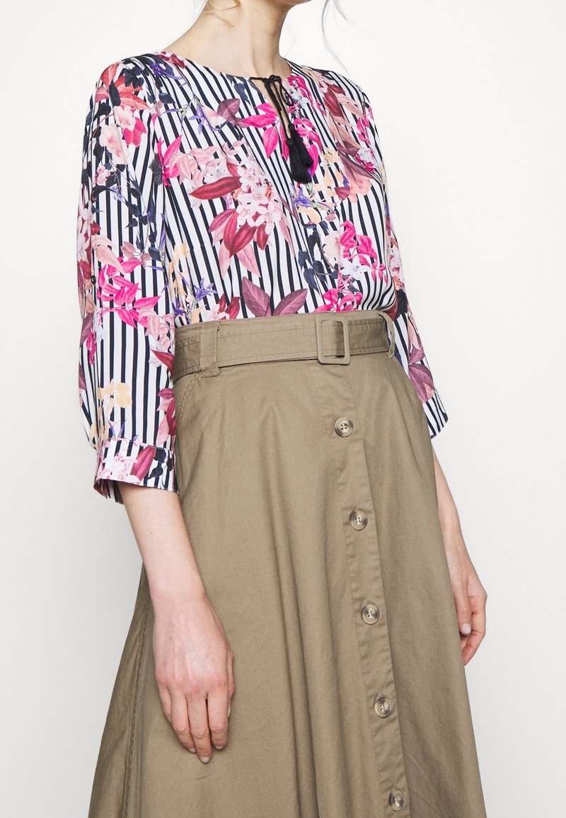 Bluzka w kwiatowy wzór z czarno-białymi paskami, zestawiona z khaki spódnicą z paskiem w talii i zapięciem na guziki z przodu.