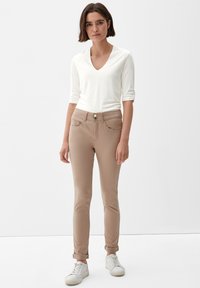 Beige slim-fit-housut, joissa on etutaskut ja nappikiinnitys, yhdistetty valkoiseen v-pääkaukotoppiin pitkällä hihalla. Teksturoitu kangas ja käärityt hihansuuhteet.