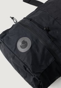 Schwarzer Rucksack aus strapazierfähigem Stoff mit glatter Textur. Besitzt ein kreisförmiges Logo, eine Reißverschlusstasche und verstellbare Riemen.