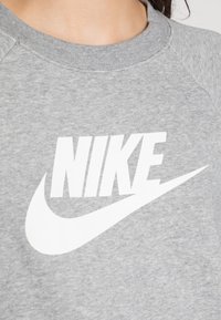 Grå sweatshirt med en vit Nike-logotyp på framsidan. Tillverkad av mjukt tyg med rundad hals och raglanärmar.