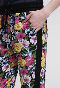 Bloemrijke joggerbroeken met een zwarte basis en levendige roze, gele en blauwe bloemen. Elastische tailleband en zijzakken met zwarte accenten.