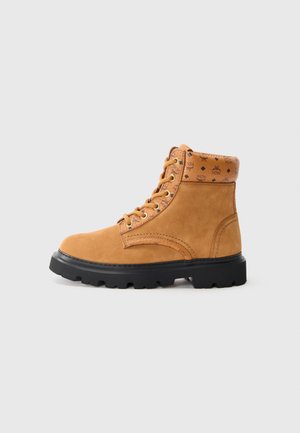 Tan leather ankle boot with a padded collar featuring a patterned design, metal eyelets, and a black rubber sole with tread detailing.