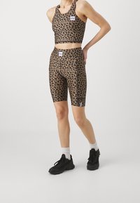 Sportowa biustonosz w print w panterkę i dopasowane szorty rowerowe w odcieniach brązu i czerni. Oba elementy mają naszywki z logo i dopasowany krój.