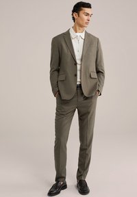 Olivno zeleno smoking z teksturirano površino, ki ima enojno zapenjanje, izrezane reverje in hlače slim fit. Nositi z lahnim kremnim polo majico.