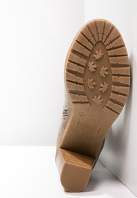 Suela de bota de ante marrón con una parte inferior de goma texturizada que presenta patrones en forma de estrella y un tacón grueso. Superficie plana para estabilidad.
