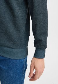 Felpa blu scuro con un motivo a maglia texturizzato, polsini e orlo a coste. Abbinata a jeans in denim blu chiaro. Design semplice e vestibilità comoda.