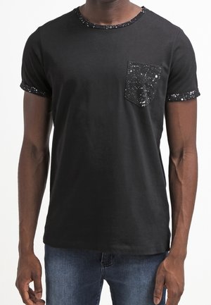 T-shirt noir à manches courtes, doté d'une poche noire texturée avec un motif tacheté. L'encolure arrondie et les poignets sont ornés.