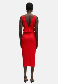 Rode jurk met V-rug en gelaagde ruches aan de taille, aansluitende silhouette, knielang, textiel met structuur en geen zichtbare patronen.