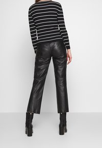 Schwarze Lederhosen mit geradem Schnitt. Kombiniert mit einem schwarz-weiß gestreiften Rippenpullover. Klobige schwarze Stiefel mit Absatz.
