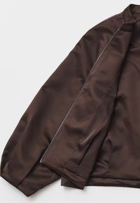 Bruin satijnen jasje met een slank ontwerp, voorzien van een ritssluiting en een gladde textuur. De mouwen zijn licht opgeblazen bij de schouders.