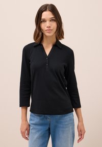 Polo-shirt noir à manches longues avec col, trois boutons à l'avant, en tissu lisse, associé à un jean en denim bleu clair.