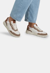 Tenisice s bijelim kožnim tijelom, smešnim suedinim akcentima i smešnim petnim tabom. Imaju teksturiranu outsole i klasični dizajn vezanja.