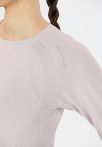 Helle rosa Sportshirt mit langen Ärmeln und geripptem Textur auf der Schulter sowie einem grauen "ENDURANCE"-Logo am Halsausschnitt. Glatte Stoffoberfläche.