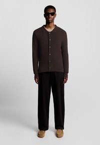 Brun cardigan med en texturerad yta, knäppning framtill och krage. Åtsidan med svarta byxor och beige mokasiner.