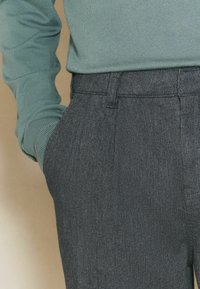 Green ribbed long-sleeve top paired with dark gray pinstriped trousers. Trousers feature a side pocket and tailored fit.