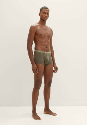 Boxer da uomo verde oliva con vestibilità aderente e vita elastica, decorata con il logo "TOM TAILOR". Il modello è in piedi a piedi nudi su uno sfondo neutro.