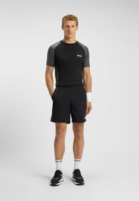 Svart idrottströja med grå ärmar, kombinerad med svarta shorts. Utsmyckad med logodetaljer och bärs med vita strumpor och svarta sneakers.