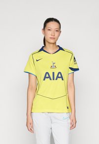 Nike nogometna majica u svijetložutoj boji s tamnoplavim detaljima, koja ima ispis "AIA" na prednjoj strani i logo ispod ovratnika. Kratki rukavi.