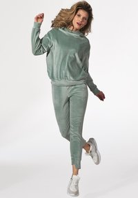 Jasnozielony dres z weluru, składający się z bluzy z kapturem i zwężających się spodni. Teksturowana tkanina, elastyczne mankiety, w połączeniu z białymi trampkami.