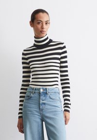 Gestreepte coltrui in zwart en wit met lange mouwen, gemaakt van een ribbelgebreide stof. Gekleed met lichtblauwe high-waisted jeans.