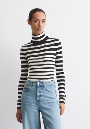 Gestreifter Rollkragenpullover in Schwarz und Weiß mit langen Ärmeln, aus einem gerippten Strickstoff gefertigt. Kombiniert mit hellblauen High-Waist-Jeans.