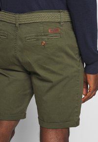 Shorts vert olive en coton avec une ceinture tissée. Dispose d'un écusson de marque en cuir et d'une poche arrière avec un bouton. Design à ourlet retroussé.
