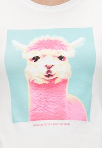 T-shirt blanc avec un graphique coloré d'un lama aux fourrures rose et blanche sur fond bleu clair, avec du texte en dessous.
