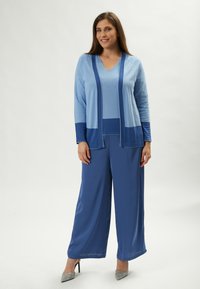 Blaues Strick-Cardigan- und Top-Set mit weit geschnittenen Hosen in verschiedenen Blautönen. Strukturiertes Material mit lässiger Passform. Funkelnde Absätze.
