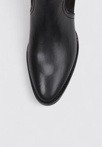 Bota de cuero negro con punta afilada, con una textura suave y un brillo sutil. Sin herrajes ni patrones visibles.