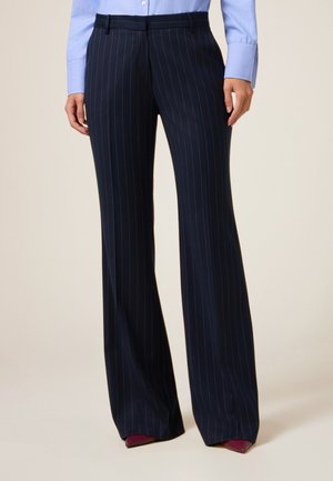 Pantalones de rayas en azul marino con un ajuste entallado, pierna ancha y parte delantera plana, hechos de una tela suave. Se llevan con una camisa azul claro y tacones.