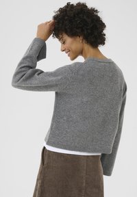Gray knitted sweater with a round neckline, cropped design, and ribbed cuffs. Worn over a white shirt and paired with a corduroy skirt.
