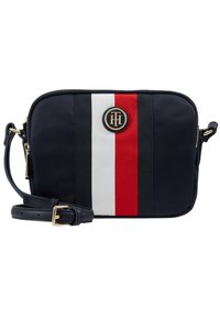 Kassi navy dengan perangkat keras emas, menampilkan desain garis tengah merah, putih, dan hitam serta logo bulat di bagian depan.