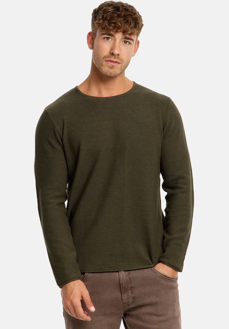 Maglione a maniche lunghe di colore verde oliva in maglia con un motivo testurizzato, design a scollo rotondo e polsini aderenti, abbinato a pantaloni marroni.