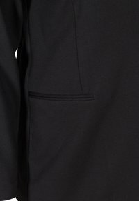 Giacca nera con una texture liscia, dotata di una tasca sul petto con dettagli di cucitura sottili. Il design è semplice e moderno.