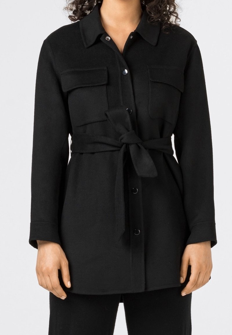 Svart, långärmad skjortjacka med två bröstfickor, ett bälte i midjan och knäppning fram. Mjuk, texturerad tyg.