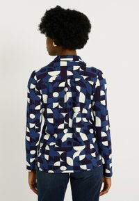 Chemise à boutons avec un motif géométrique en marine, blanc et bleu clair, avec un col et une coupe décontractée. Tissu doux et texturé.