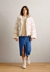 Doudoune beige clair, pull en maille torsadée crème, jupe en denim avec fente sur le devant, baskets blanches. Design minimaliste avec textures douces.