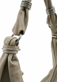 Handvat van een olijfgroene leren handtas met gedraaide stof en metalen ringen, met een gladde textuur en een gedrapeerd designelement.