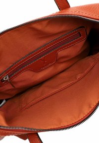 Innenleben der Lederhandtasche in Orange mit Reißverschluss. Verfügt über eine Reißverschlusstasche und glattes Stofffutter. Akzente sind die kontrastierenden Nähte.