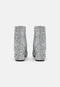 Botines plateados brillantes con una superficie texturizada, un tacón alto en bloque y un borde superior suave, que cuentan con una cremallera en la parte posterior.