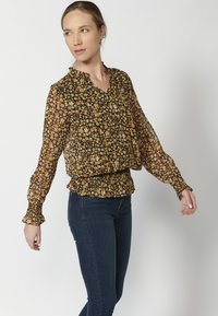 Blusa nera floreale con scollatura a V, maniche lunghe, vita smock, caratterizzata da fiori arancioni, gialli e rosa su un tessuto trasparente.