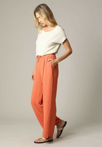 Lichtgewicht crème top met een ronde hals, gecombineerd met losvallende, gestructureerde koraaloranje broek met een elastische tailleband en zakken.