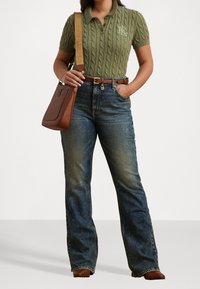 Zelený pletený polo tričko s krátkým rukávem, vysoké modré džíny v jemném umytém stylu, hnědý kožený pásek a hnědá kabelka přes rameno.