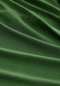 Tissu vert avec des plis doux et une texture subtile, montrant un drapé lisse et un motif tissé fin à la lumière naturelle.