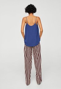 Haut sans manches bleu avec des fines bretelles, associé à un pantalon ample rayé bordeaux et crème, mettant en avant un tissu doux et une silhouette décontractée.
