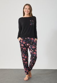 Μαύρη μπλούζα με μακριά μανίκια και λουλουδάτη τσέπη, συνδυασμένη με μαύρο παντελόνι με λουλουδάτο μοτίβο. Και τα δύο είναι φτιαγμένα από μαλακό ύφασμα με άνετη εφαρμογή.