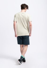 T-shirt beige clair, en coton, à manches courtes. Assorti à un short bleu marine, avec poches latérales. Chaussures noires avec semelles blanches.