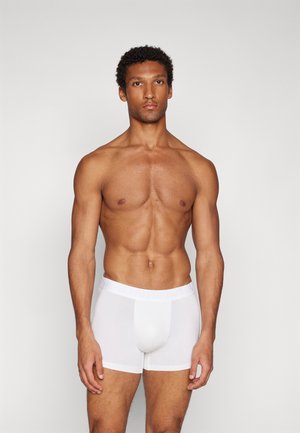 Weißer Baumwoll-Boxerbrief mit einem weichen Bund, der eine glatte Textur und eine enganliegende Passform aufweist, präsentiert an einem männlichen Modell.