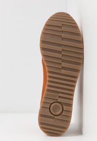 Brun gummiyttersida med texturerat mönster, med ett cirkulärt designelement. Sidan visar "Gabor"-logotypen, med detalj "Tillverkad i Slovakien".