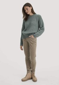 Hellgrüner, strukturierter Strickpullover mit rundem Ausschnitt; kombiniert mit beigen Cordhosen und braunen Plateauschuhen mit Reißverschlüssen.